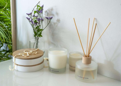 Decorative candles, a box with a string of pearls, wooden sticks in a glass jar, and a vase with purple flowers.