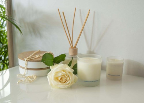 A white rose, candles, a container with reed diffusers, and a jewelry box with a pearl necklace.