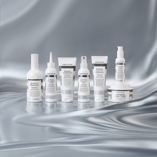 A collection of white skincare products with black text, arranged on shiny silver fabric background.