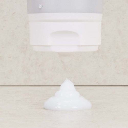 Wit schuim komt uit een muurbevestigde dispenser op een oppervlak.