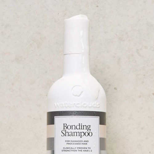 Eine weiße Flasche mit Pumpkopf, bezeichnet 'Bonding Shampoo' für beschädigtes Haar, mit grau-schwarzem Etikett.