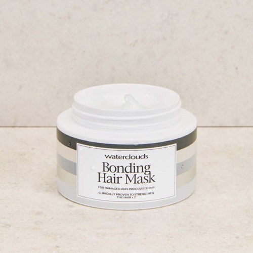 Een witte container van Waterclouds Bonding Hair Mask met zwarte en zilveren strepen, gedeeltelijk geopend met de crème binnen.