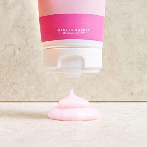 Een roze en witte tube die roze crème op een vlakke ondergrond spuit.