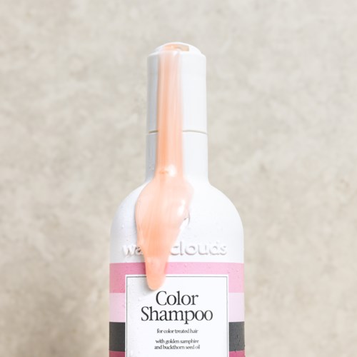Een witte flesje met kleurschampoo met roze en zwarte etiketten, met wat perzikkleurige vloeistof die van de top druppelt.