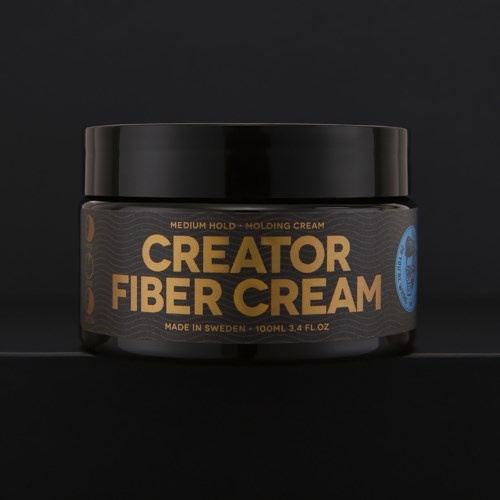 Ein schwarzer Behälter mit der Aufschrift 'Creator Fiber Cream' mit goldenen und blauen Details, auf schwarzem Hintergrund.