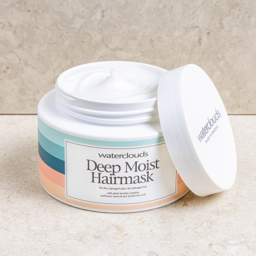 Een ronde container met diepe vochtinbrengende haarmasker met witte crème, gelabeld "Waterclouds" op een beige oppervlak.