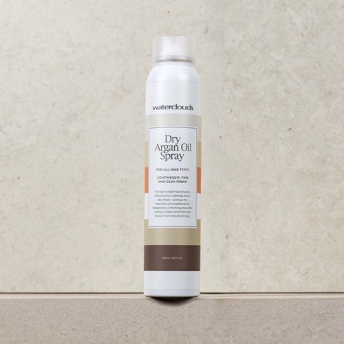Een witte sprayfles met label 'Waterclouds Dry Argan Oil Spray' staat tegen een eenvoudige achtergrond.