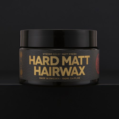 Een zwarte container met Hard Matt Hair Wax, met gouden en rode tekst en ontwerp op een donkere achtergrond.