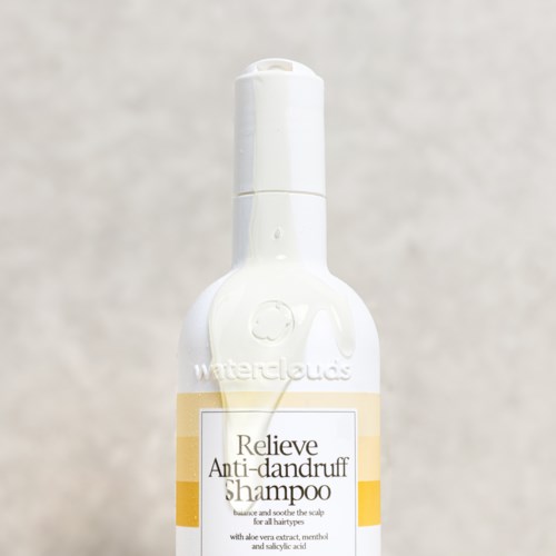 Een witte sprayfles met een label dat zegt 'Relieve Anti-dandruff Shampoo' en een gele streep.