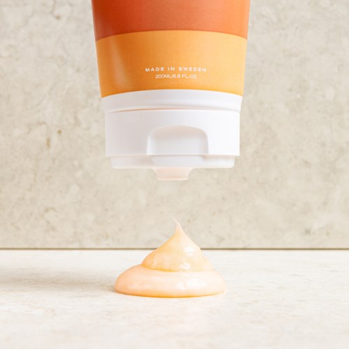 Een tube wordt ingedrukt, waardoor een spiraal van oranje crème of lotion op een plat oppervlak verschijnt.