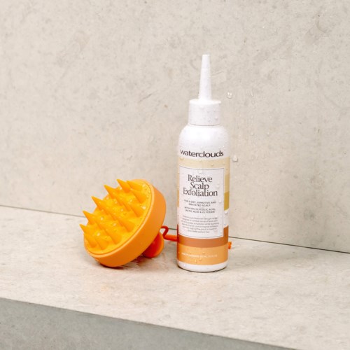 Een flesje hoofdhuid exfoliatieproduct met een gele massageborstel op een badkamertafel.