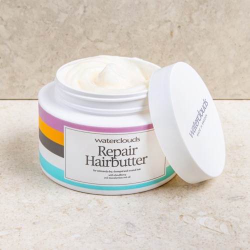 A jar of waterclouds Repair Hairbutter with the lid open, showing white cream inside.