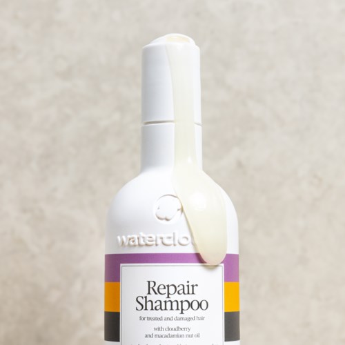 Witte fles voor Repair Shampoo voor beschadigd haar, met paarse, gele en zwarte strepen.