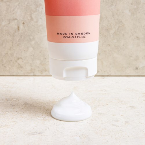 Een roze en wit tube, gemarkeerd 'Made in Sweden,' spuit witte crème uit op een oppervlak.