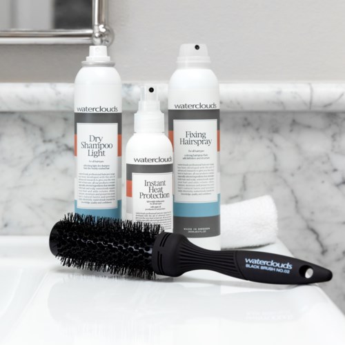 Hair care products including dry shampoo, heat protection spray, hair spray, a black round brush, and a white towel.