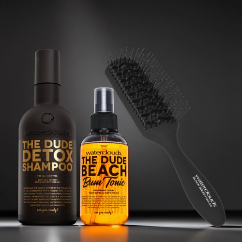 Zwei Flaschen Haarpflegeprodukte und eine schwarze Haarbürste vor dunklem Hintergrund.
