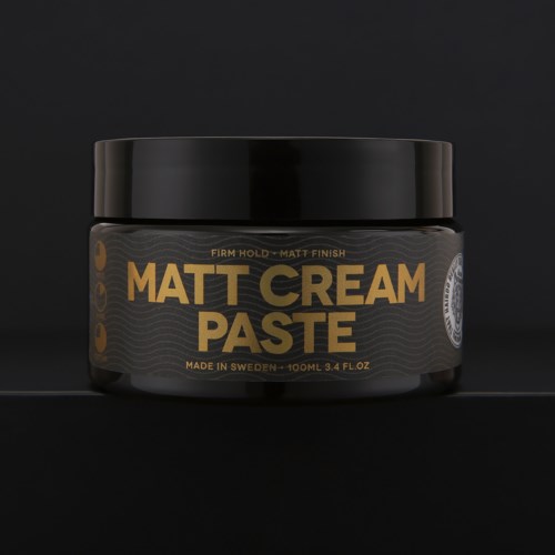 Ein schwarzer Behälter mit matter Cremepaste, goldene und graue Schrift und Design auf Etikett.