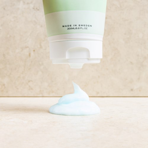 Een witte en groene tube met tekst die blauwe en witte crème of schuim op een oppervlak spuit.