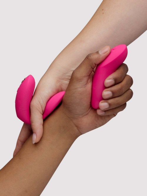 En person håller ett rosa hudvårdsverktyg med strukturerade och släta ytor och använder det på armen för hudvård.