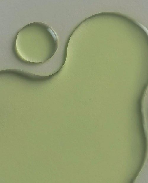 Grünliche Flüssigkeit mit zwei runden Formen und gebogenen Rändern, ähnlich Öl oder Sirup auf einer Oberfläche.