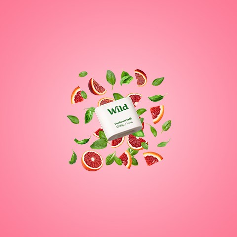 Een doos met 'Wild' erop, omringd door grapefruitpartjes en muntblaadjes op een roze achtergrond.