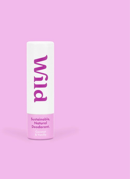 Een witte deodorantstick met paarse en roze tekst op een roze achtergrond. Het label zegt "Wild" en noemt kokos & vanille.