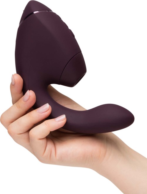 A hand holds a purple, ergonomic personal massager with a curved design and a smooth surface.