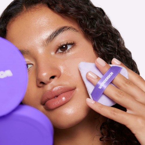 A woman with clear skin uses a white cleansing pad with a purple band that has the WordPress logo.