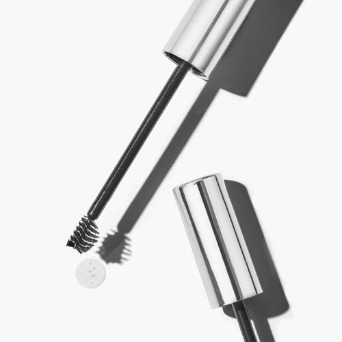 En mascaraborste med vit, silver och svart design, och ett silverlock, placerad på en vit bakgrund.