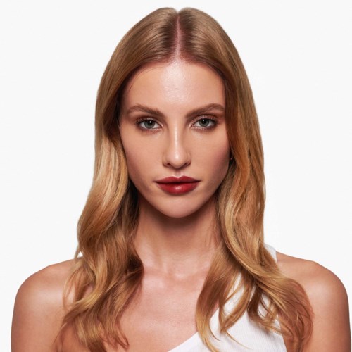 Een vrouw met lang, golvend blond haar en rode lippenstift kijkt recht in de camera.
