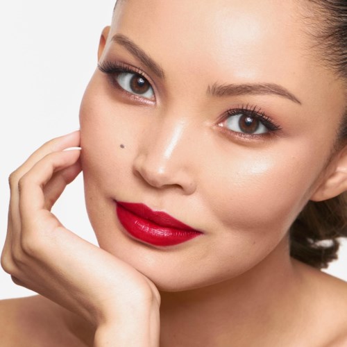 Close-up van een vrouw met een glad huid, heldere ogen en rood lippenstift, die haar gezicht aanraakt.