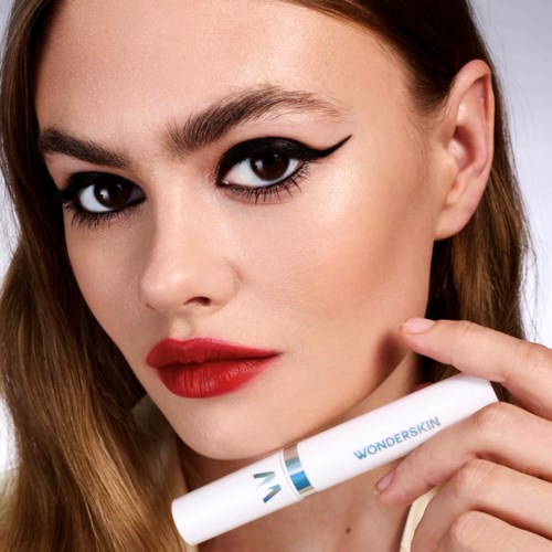 Eine Frau mit auffälligem Make-up, rotem Lippenstift, schwarzem Lidstrich, die ein Wonderskin-Produkt hält.
