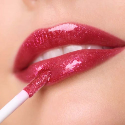 Close-up of lips applying pink gloss with a brush on shiny lips.