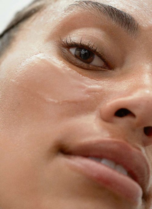 Nahaufnahme eines Frauen Gesichts mit glatter Haut, dunklem Auge und leicht geöffneten Lippen.