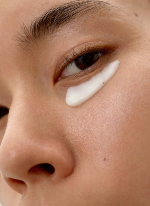 Eine Person hat eine weiße Creme unter dem Auge, Nahaufnahme, zeigt Haut und Teil der Nase.