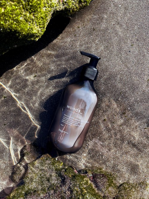 Eine braune Flasche mit Pumpen auf einem Felsen, Sonnenlicht wirft Schatten, umgeben von Moos und natürlicher Umgebung.