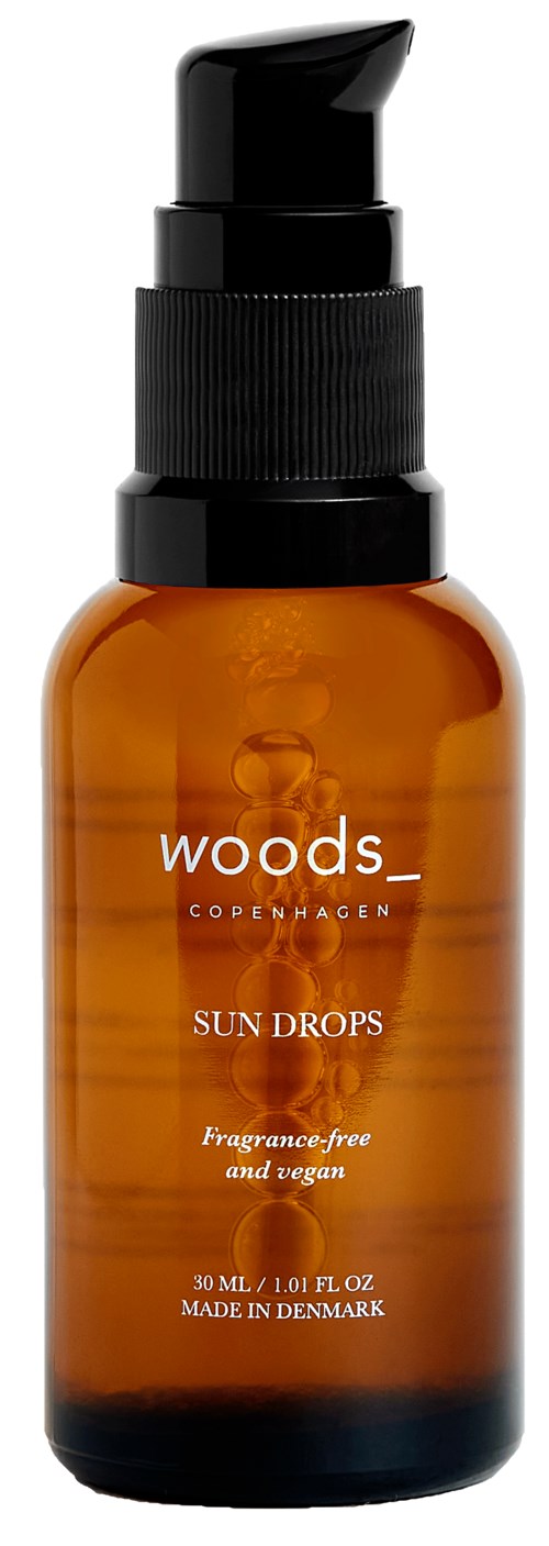 Bernsteinfarbene Flasche mit schwarzem Pumpkopf, beschriftet 'Woods Copenhagen Sun Drops', parfumfrei, vegan, hergestellt in Dänemark.