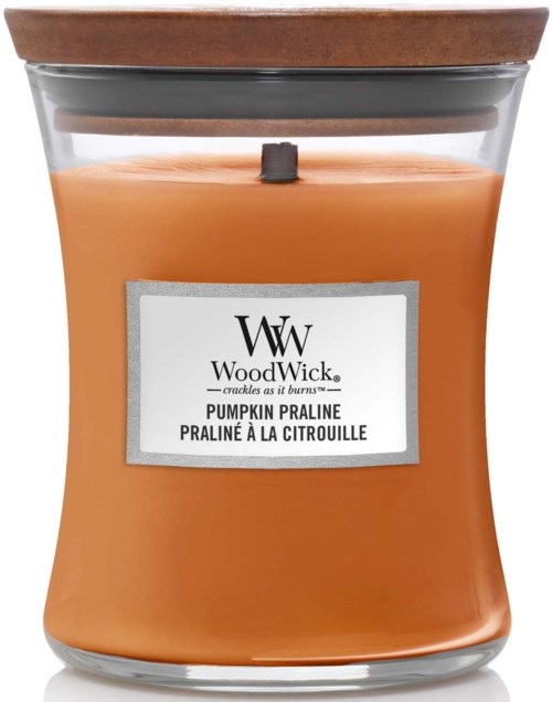 Pumpkin-värinen tuoksukynttilä lasipurkissa, jossa on puinen kansi ja etiketti, jossa lukee WoodWick, kurpitsapralinen.