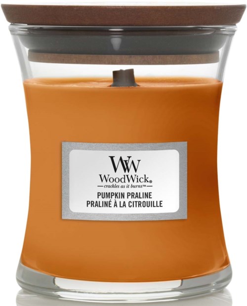 Kurpitsankeltainen kynttilä lasipurkissa, jossa puuliekki ja etiketti 'WoodWick Pumpkin Praline'.