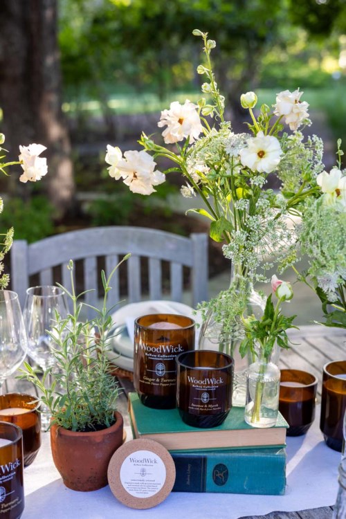 En bord med blommor, ljus, glas och en bok utomhus, i en trädgårdsmiljö.