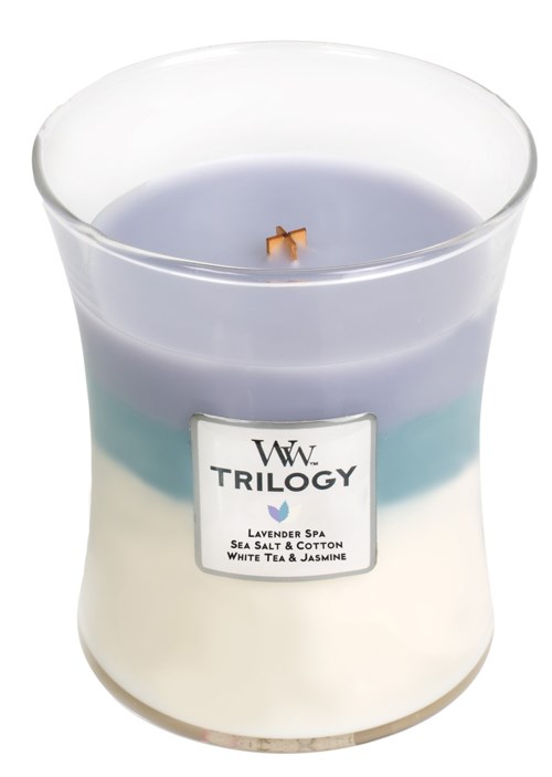 A scented candle labeled "Trilogy" with lavender, sea salt, cotton, white tea, and jasmine scent, in a glass container.
