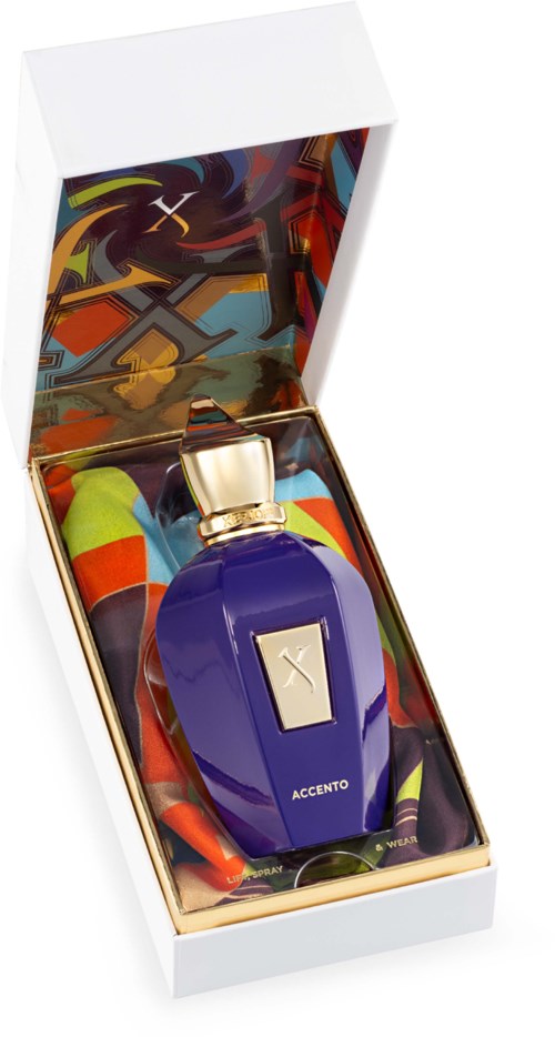 Een parfumfles in een witte doos met kleurrijk patroonstof binnenin. De fles is donkerblauw met een gouden dop.