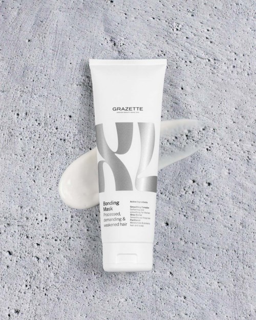 A white tube of Grazette bonding mask lies on a textured gray concrete surface with some of the cream spread nearby.