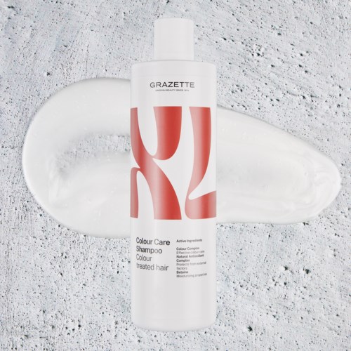 Een wit flesje GRAZETTE shampoo met roze ontwerp, ligt op een getextureerde achtergrond met een gelovige shampoo.