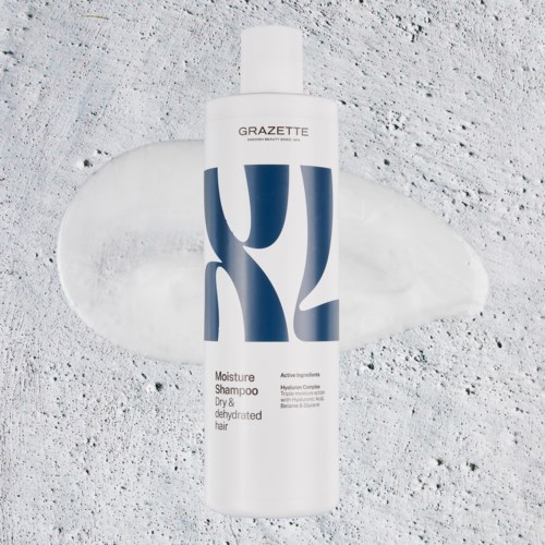 En vit flaska med fuktgivande schampo med blå och svart text på en strukturerad yta. En liten kräm eller lotion i närheten.