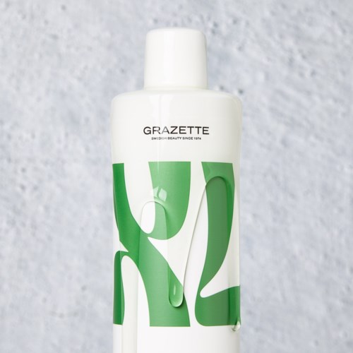 Een witte fles met groene vormen en zwarte tekst die "GRAZETTE" zegt op een grijze achtergrond.