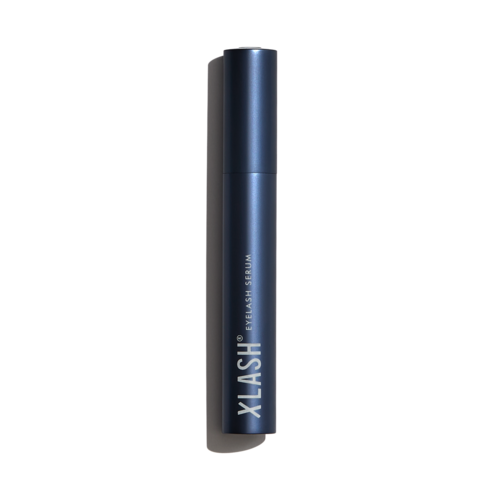 Een blauwe cilindrische tube met de tekst 'V KLASH EYELASH CREAM' staat rechtop tegen een zwarte achtergrond.