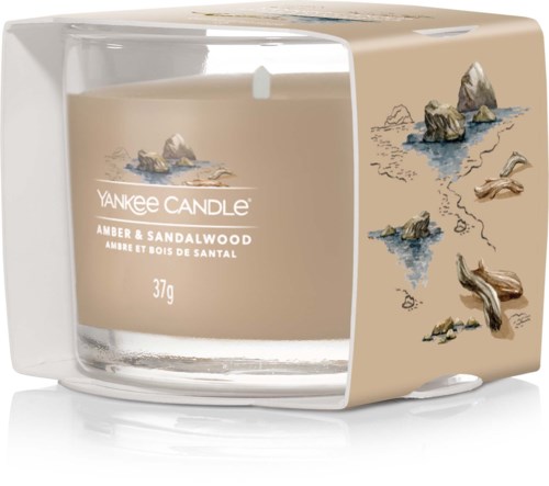 Et lys i klart glass med sand- og tresmak etikett, dekorert med små steiner og drivved illustrasjoner.