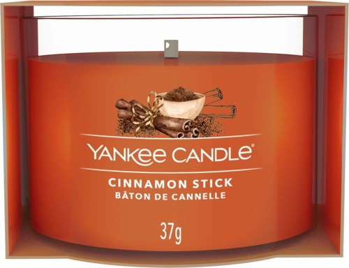 Een geurkaars met kaneelgeur van Yankee Candle, in een oranje houder, met kaneelstokken en specerijen op het label.