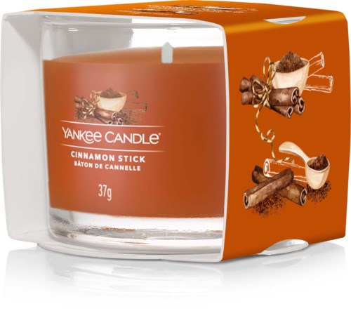 Geurkaars met kaneelgeur in een oranje container, versierd met kaneelstokjes en bruine specerijen.